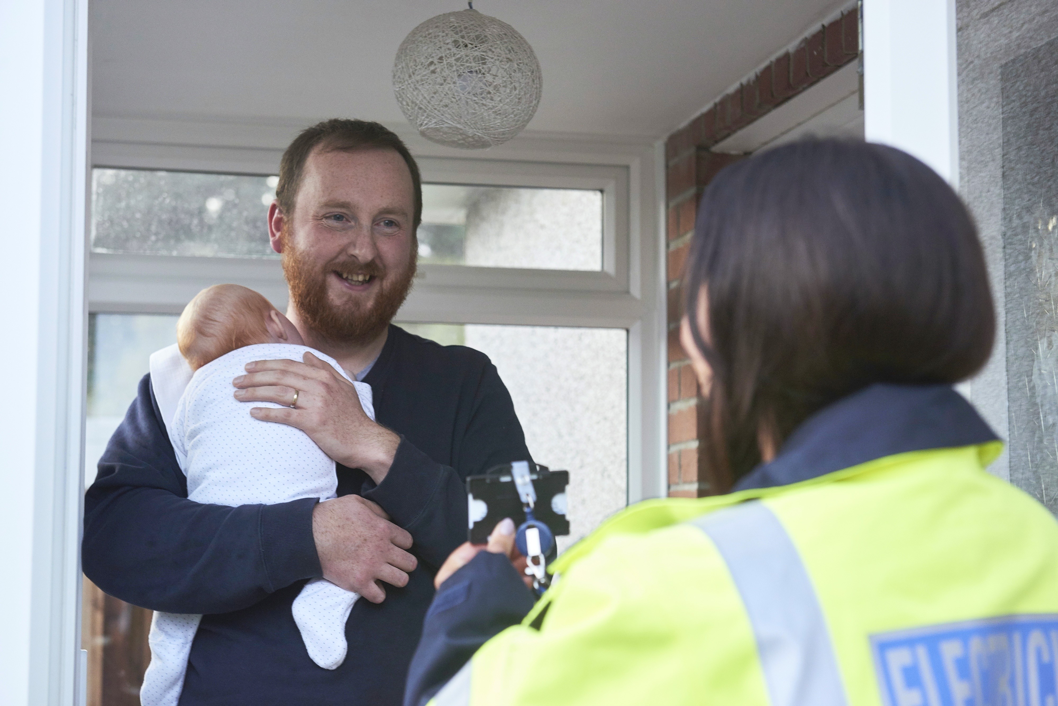 Man holding baby and smiling at woman in high vis jacket