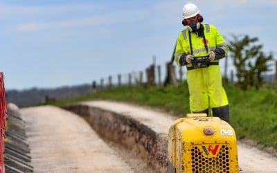 A machine digging a cable trench along a partially closed road, being operated by a man in hi-vis