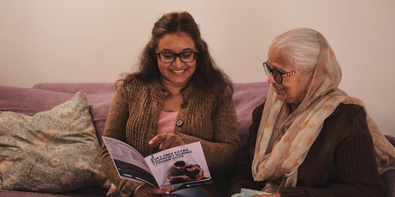 Two smiling women look at a booklet together.