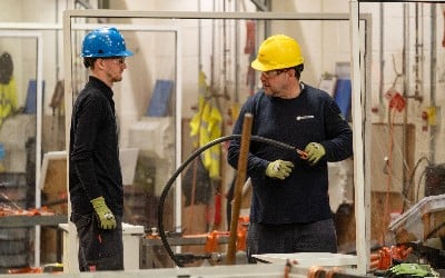 Two men in hard hats talk; one holds a cable.