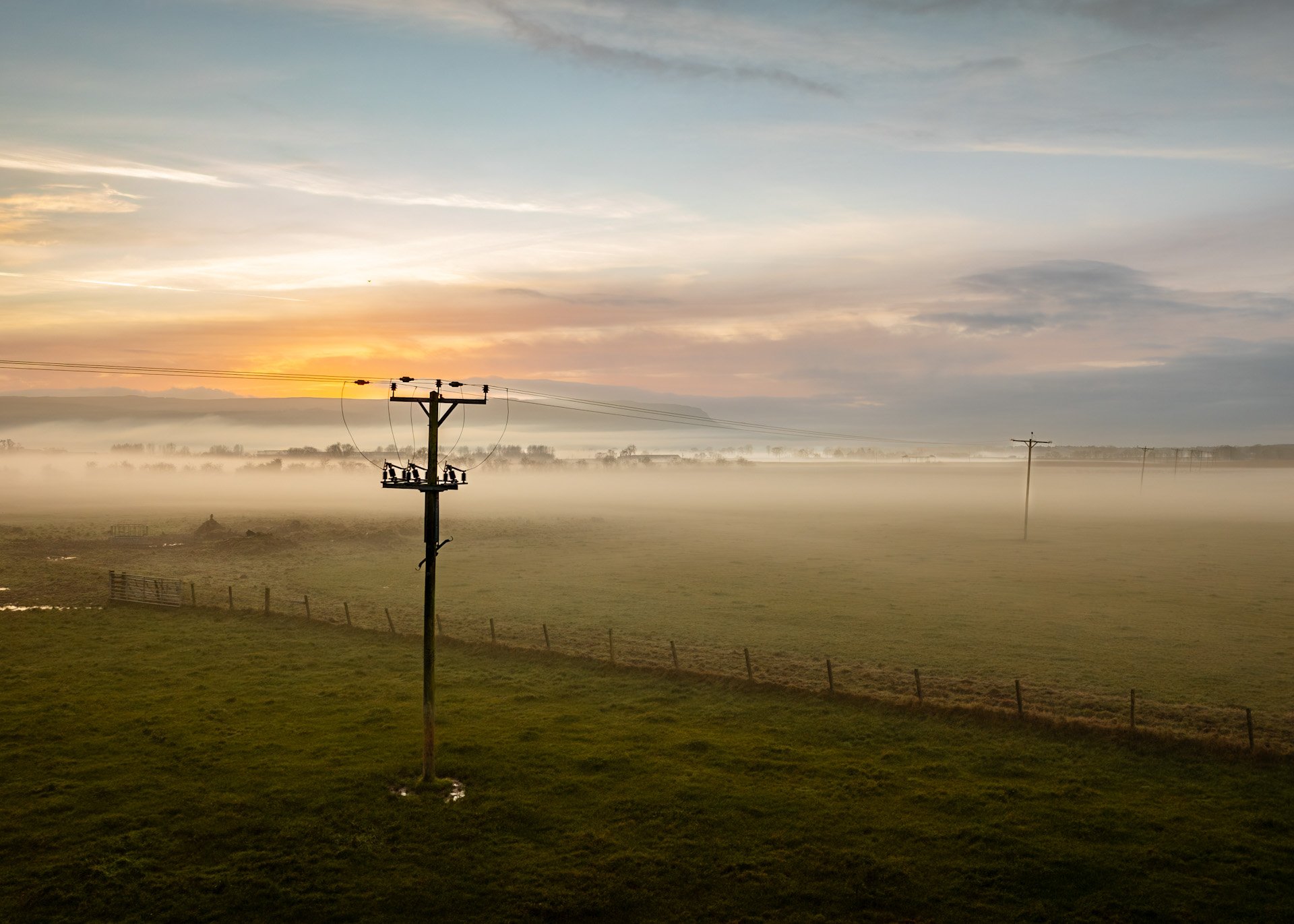 An overhead power line crossing a field of a misty morning