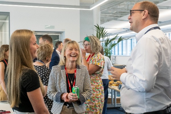 Three people conversing and laughing at an indoor gathering.