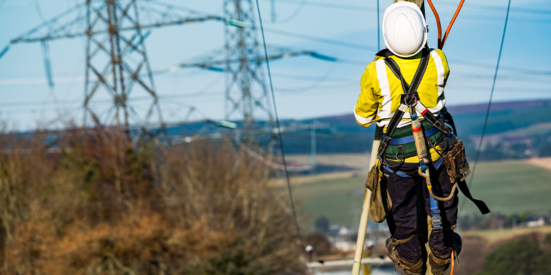 Engineer climbing pole with electricity towers in the background