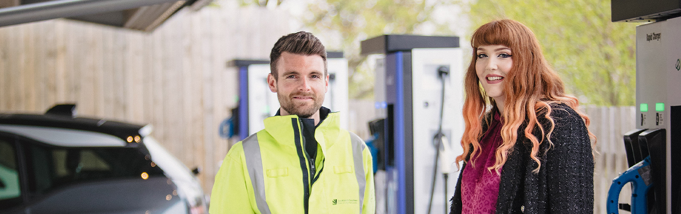 Image of engineer with customer smiling at camera next to electric vehicle