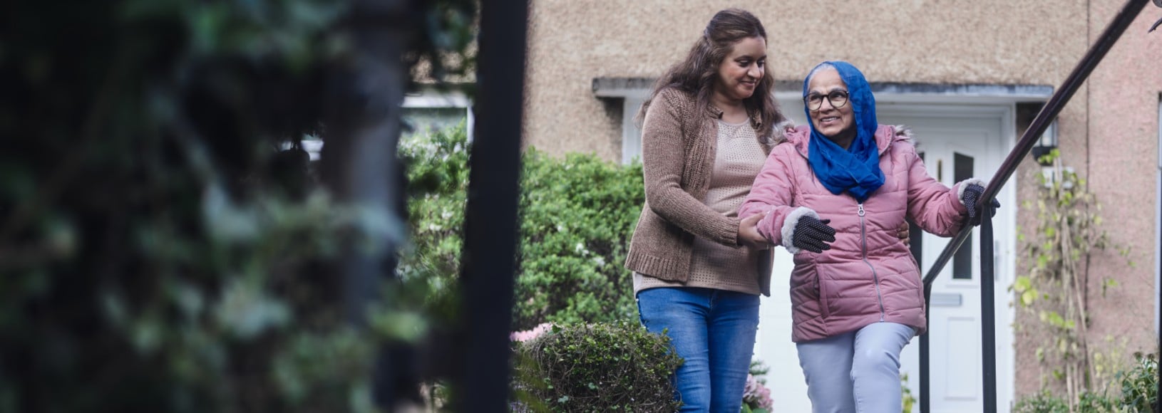 An elderly person being supported in front of their home