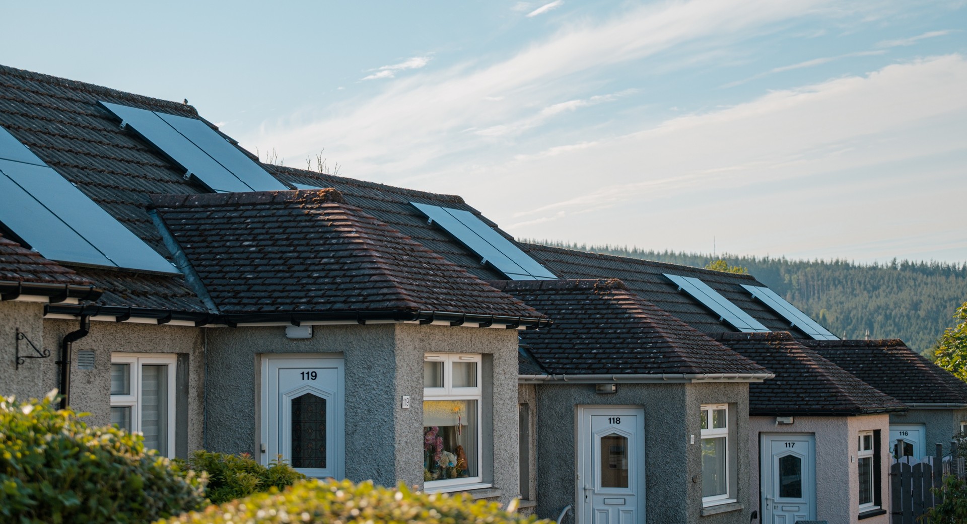 Picture of houses with solar panels on each roof. Clear blue sky and clouds in background.