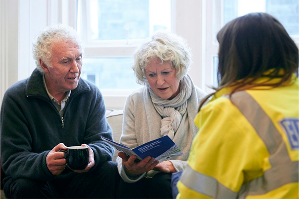 Image shows SSEN colleague showing elderly couple a sign up form 