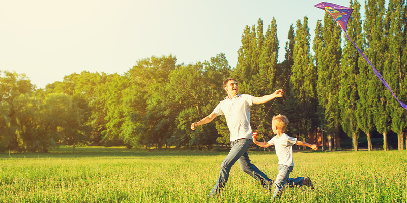 Father running with his son and their kite through a park 