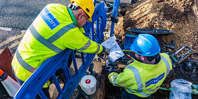 Image of SSEN engineers working in an excavated hole looking at cable plans
