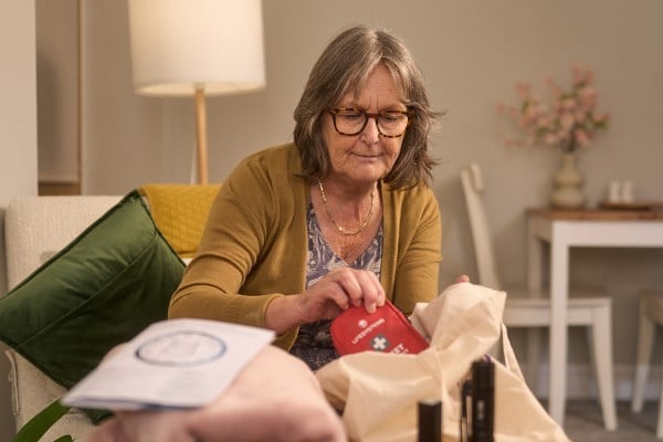 Older woman puts red first aid kit into a canvas bag.